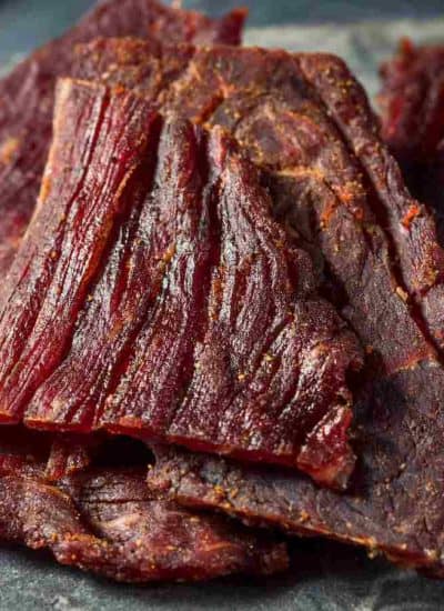 Image of several pieces of beef jerky on a dark, round slate board.