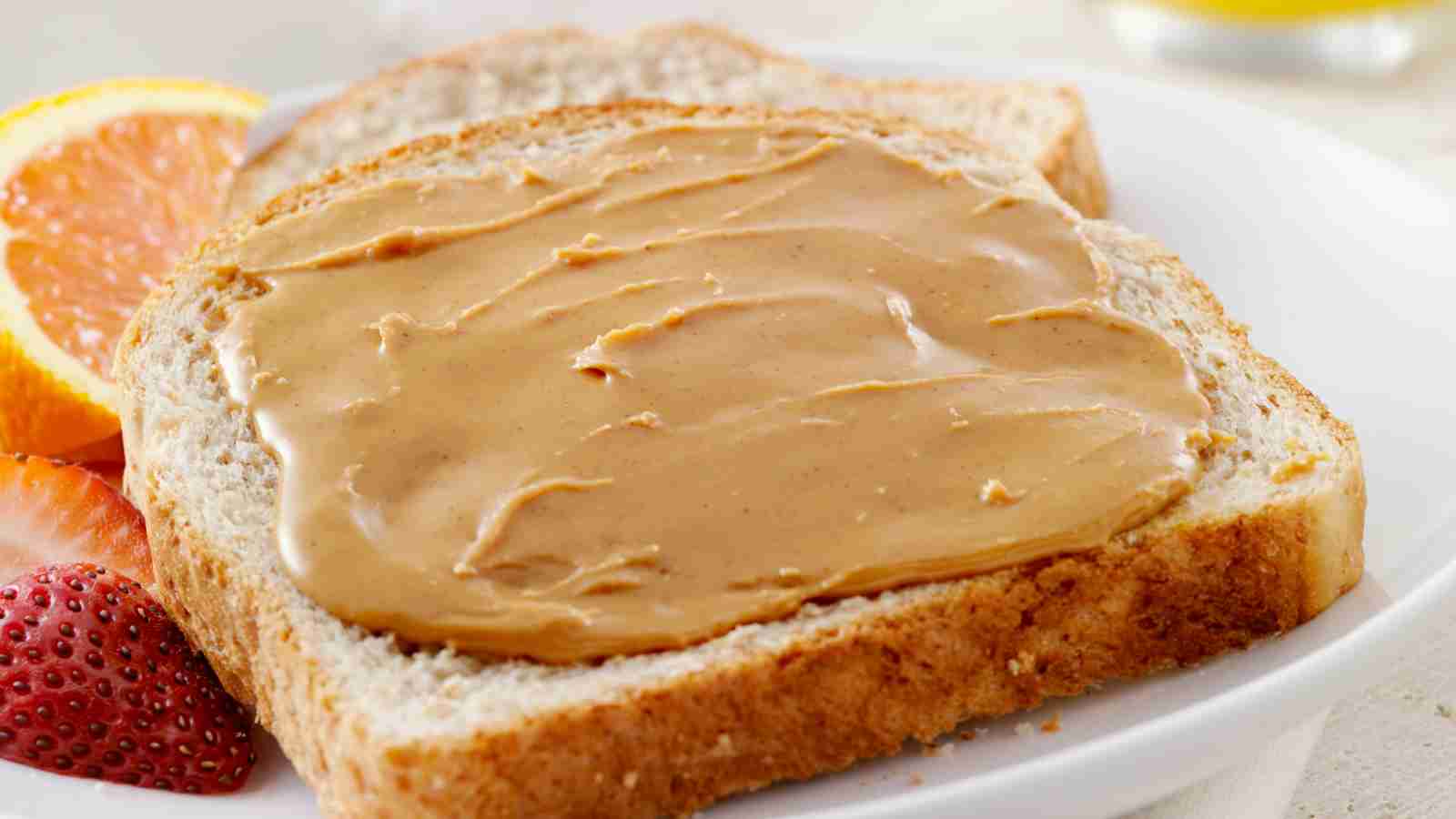 Two slices of bread with smooth peanut butter spread on top on a white plate.