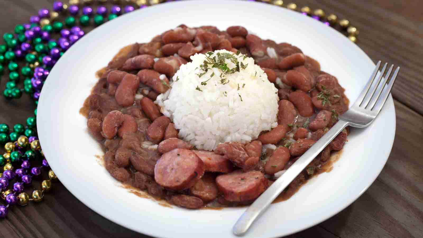 A white plate with a serving of red beans and sausage, topped with a mound of white rice garnished with herbs.