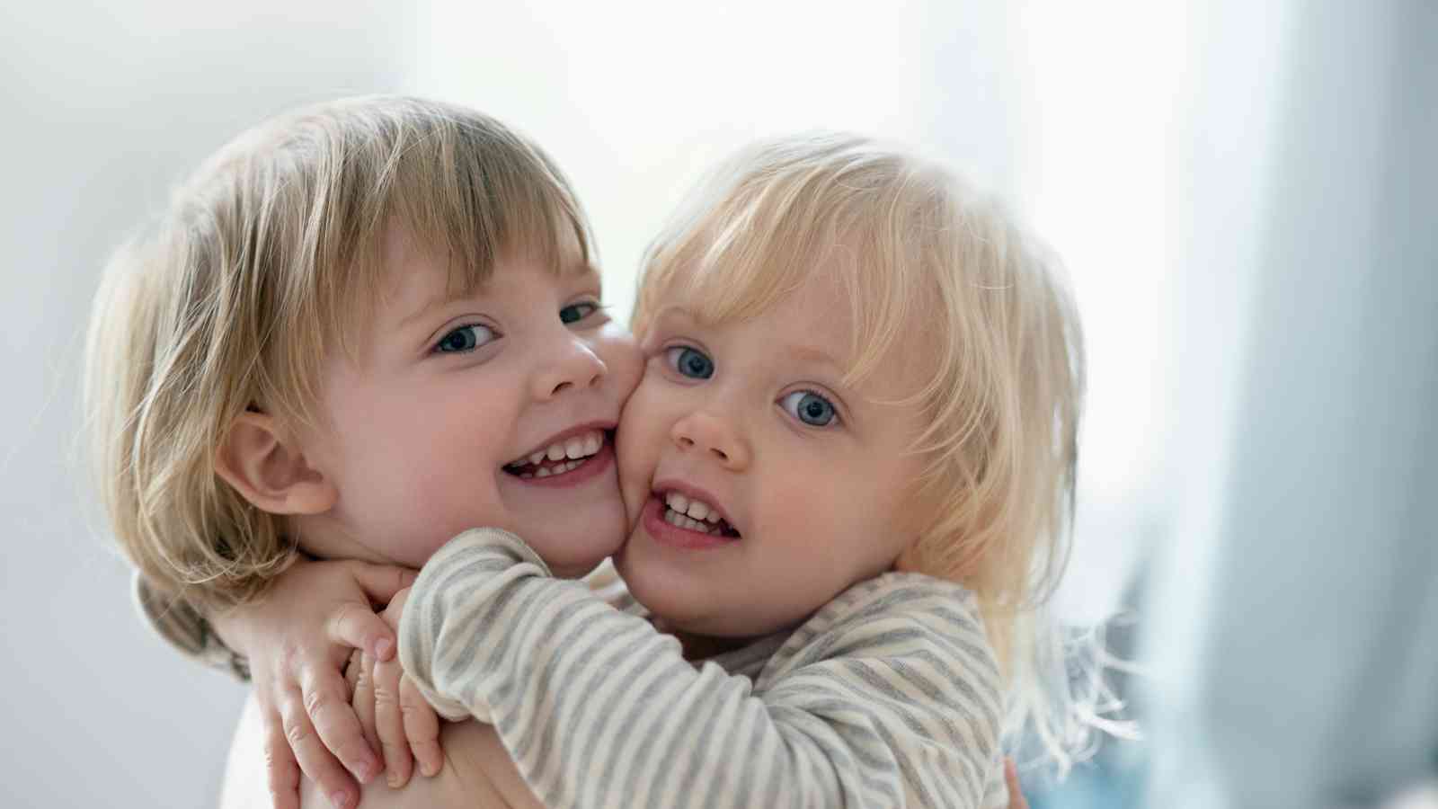 Twin baby girls with blond hair hugging each other.