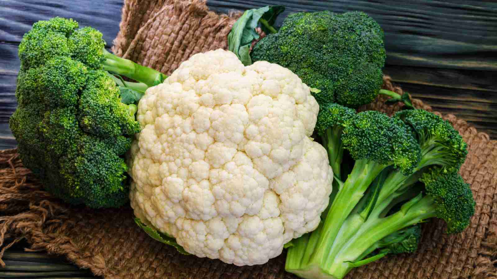 A head of cauliflower and two bunches of broccoli on a brown burlap sack.