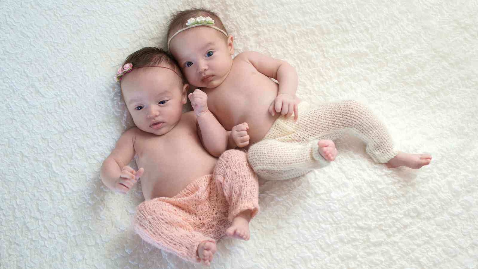 Twin baby girls laying on the bed wearing matching pants and headband.