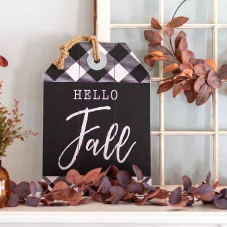 A shelf displays autumn-themed decorations including a "Hello Fall" sign, brown bottles with leaves, and a wreath of brown leaves hanging on an old window frame.