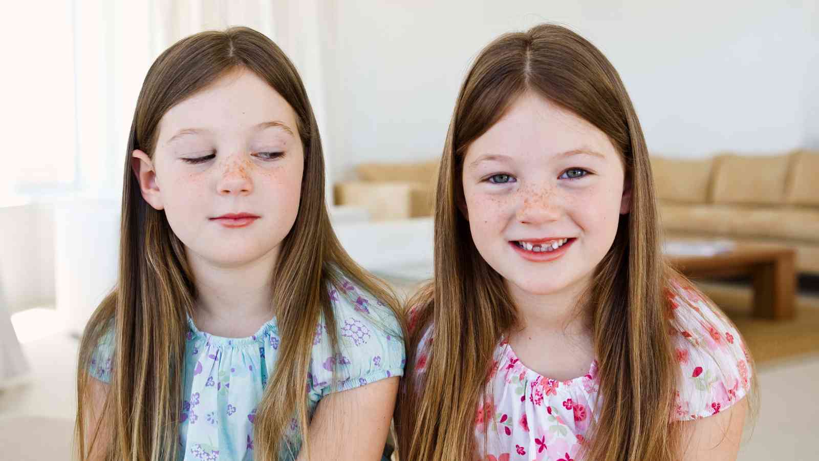 Twin girls, one smiling and the other one is looking down.