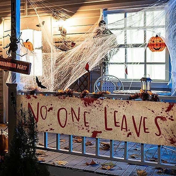 A front porch with Halloween decorations, including a “No One Leaves” banner, fake spider webs, and various ornamental pumpkins and lanterns.
