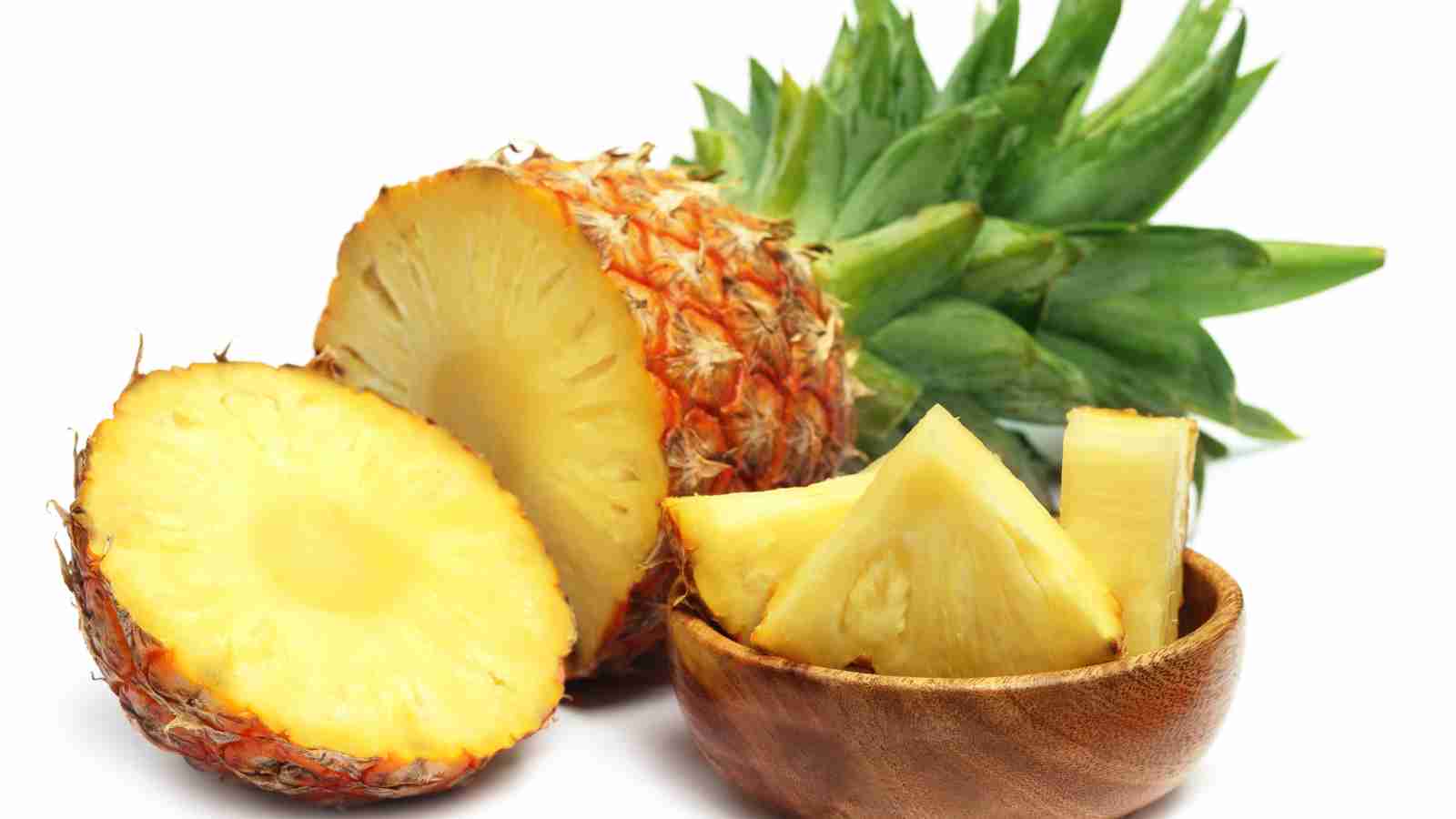 A pineapple cut in half and a wooden bowl with slices of pineapple in it.