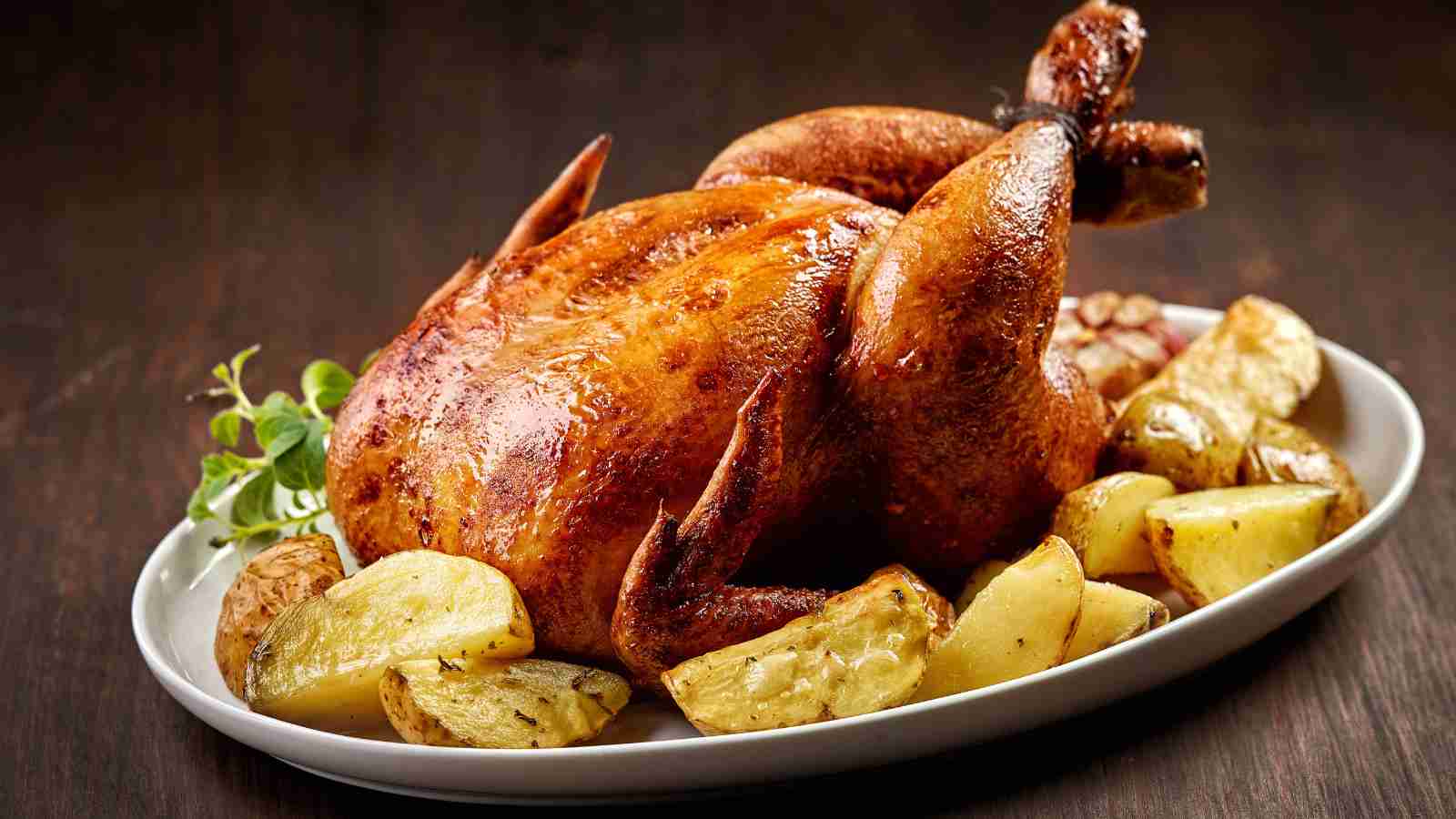 A whole roasted chicken on a white plate surrounded by roasted potatoes.
