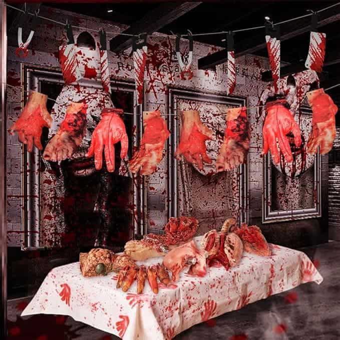 Horror-themed display featuring severed and bloodied mannequin hands hanging and a table covered with bloodied fake organs.