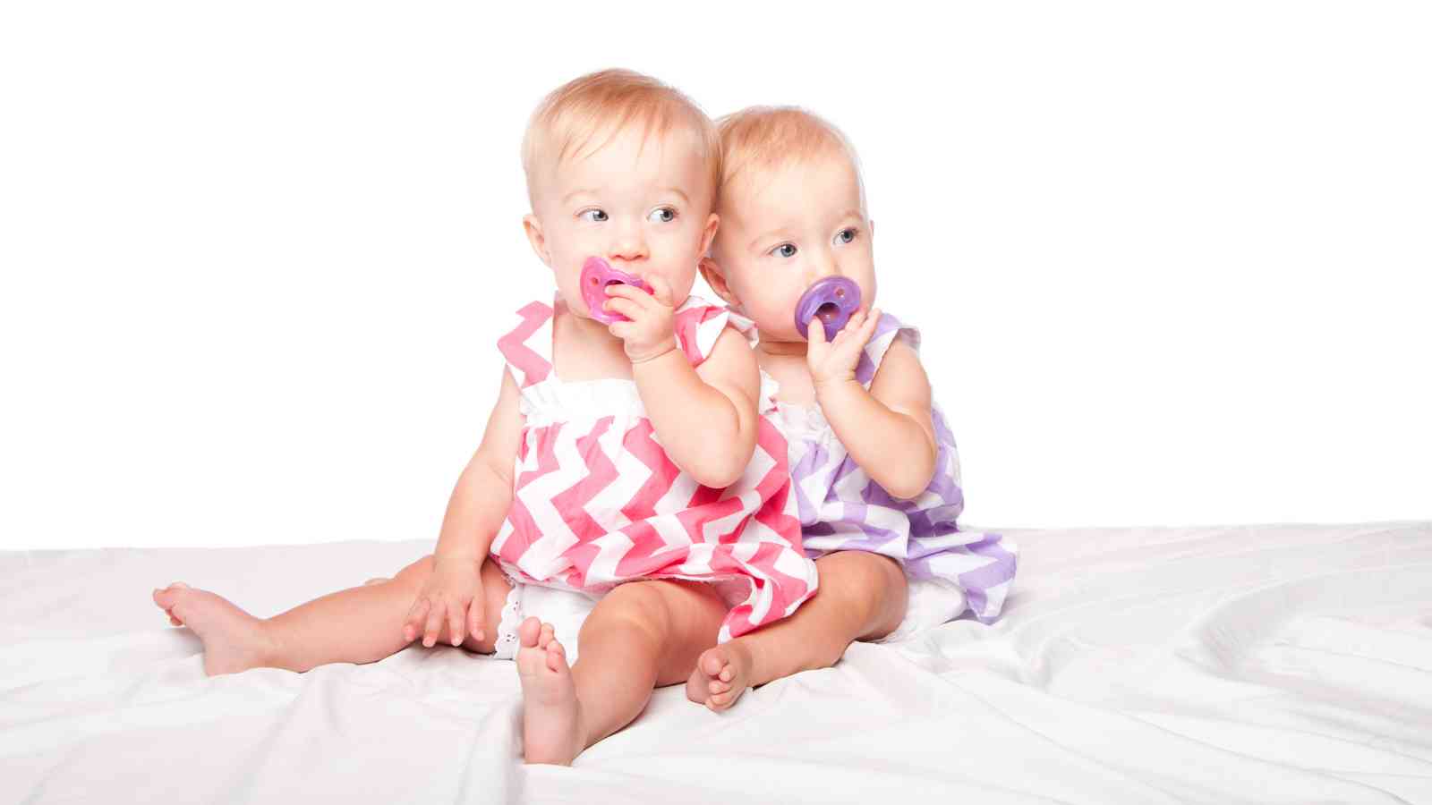Twin baby girls sucking on their pacifier.