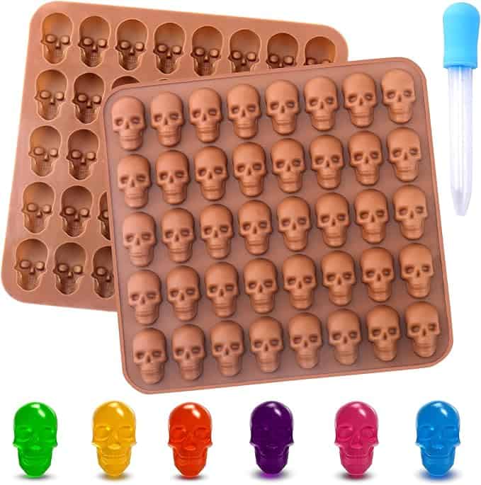 Two silicone molds with skull shapes, a plastic dropper, and colored skull-shaped items displayed: green, yellow, red, purple, and blue.