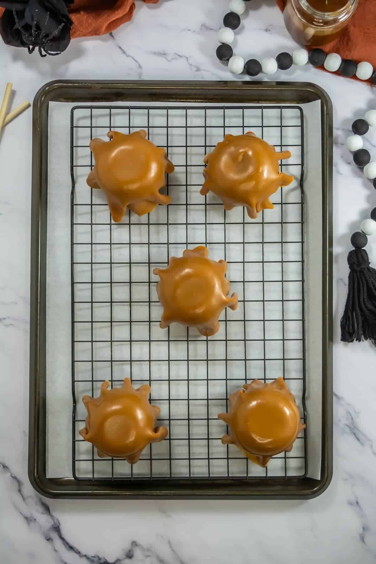 Five caramel-covered apples on a wire rack on top of a baking sheet with parchment paper.