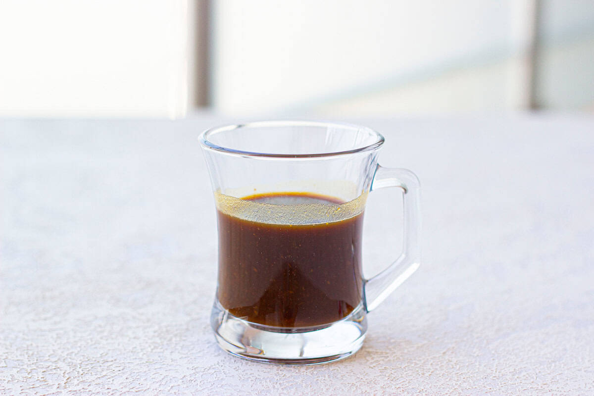 A clear glass mug filled with dark coffee sits on a textured white surface.