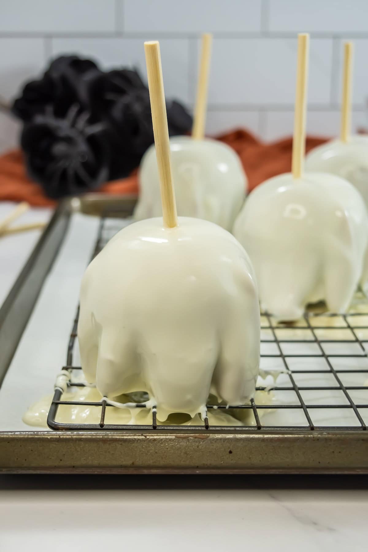 Four white chocolate-covered apples skewered with sticks in the middle on a wire rack.