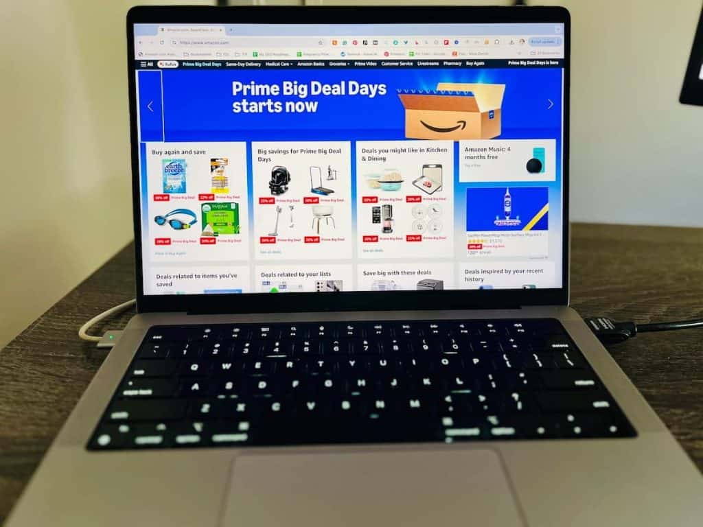 A laptop screen displays an online shopping page with "Prime Big Deal Days starts now" banner and images of various products on sale.