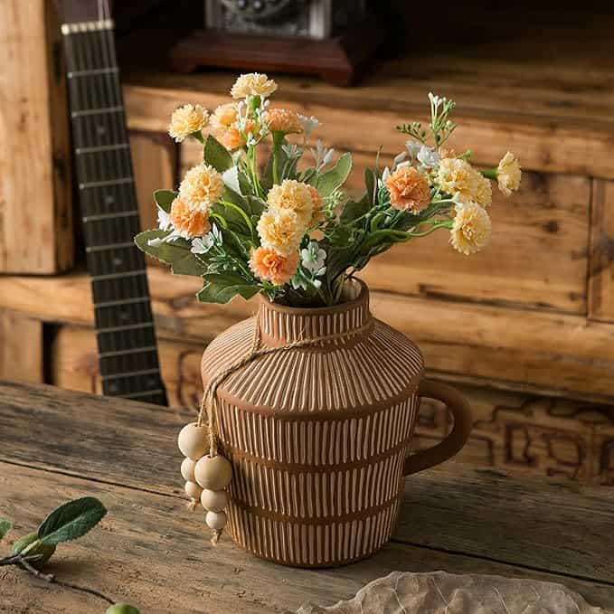 A decorative ceramic vase with a striped pattern holds yellow and orange flowers on a wooden table.