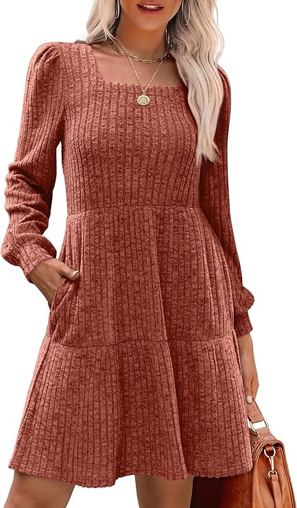 A person wearing a ribbed, rust-colored dress with long sleeves and pockets, accessorized with a necklace.