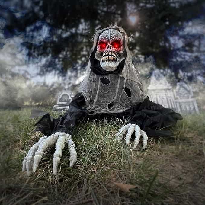 A ghoulish figure with glowing red eyes and skeletal hands crawls on grass, wearing a tattered cloak, with a graveyard and trees in the background.