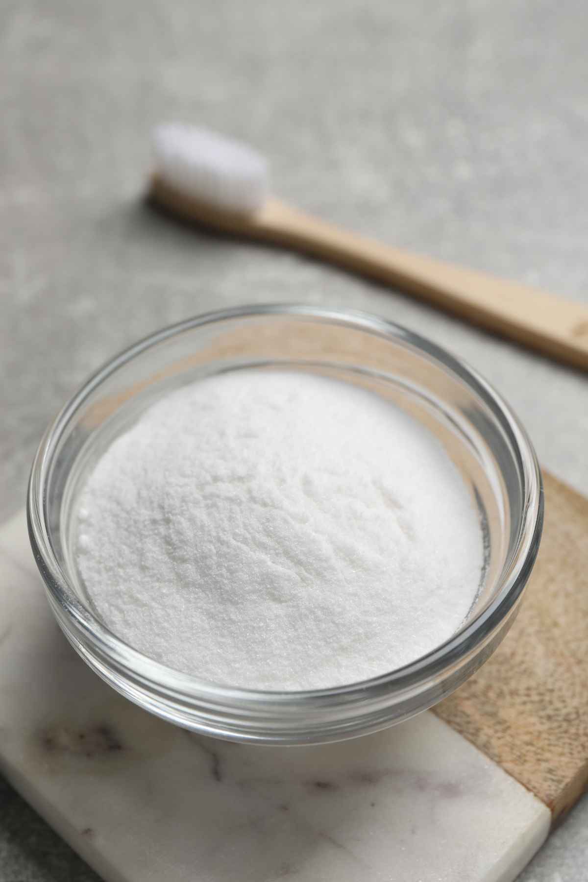 A bowl of baking soda with a toothbrush on the background.
