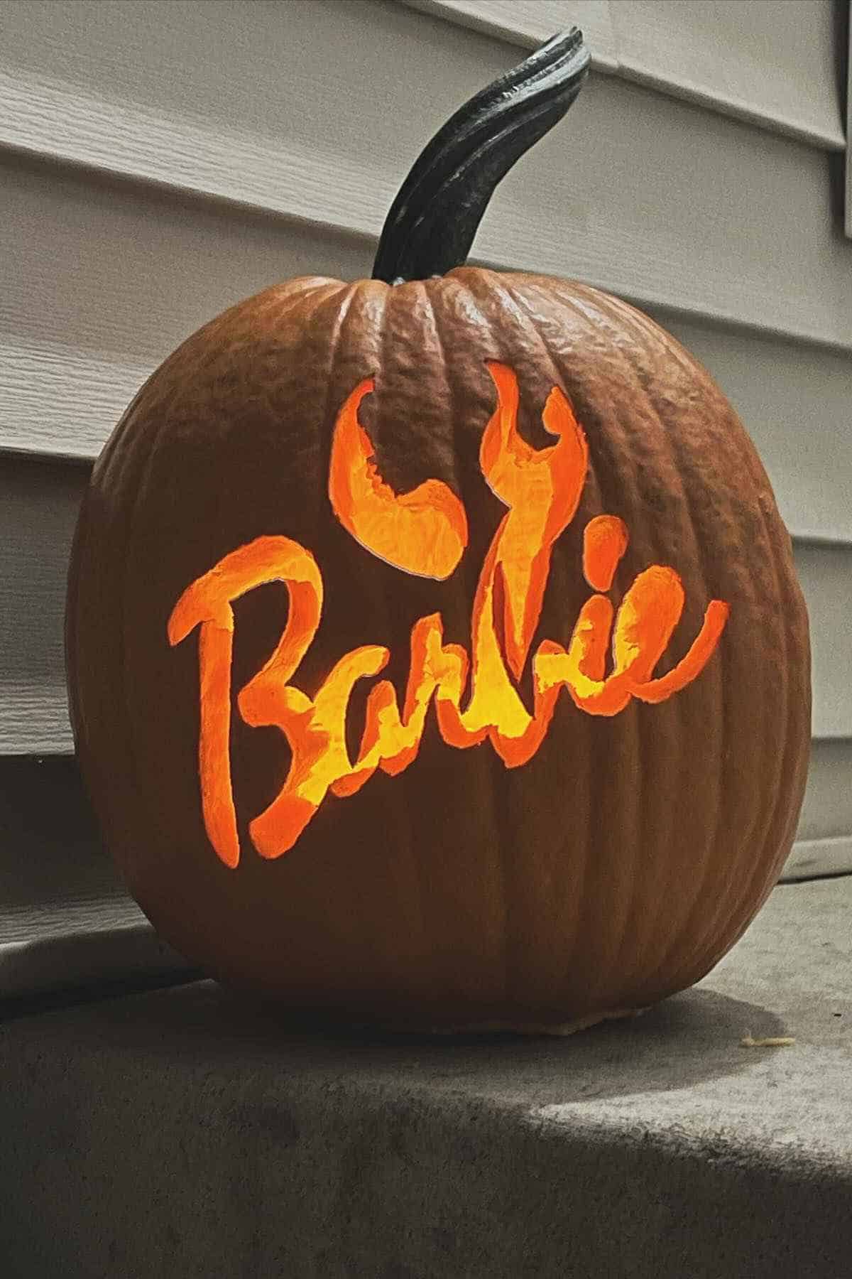Carved pumpkin with the word "Barbie" and a flame design, placed on a porch step.