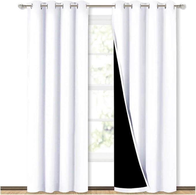 White blackout curtains hang in front of a window, partially open to reveal a bright view outside.