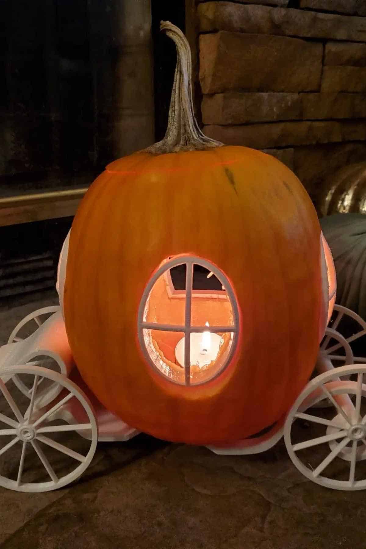 A carved pumpkin designed as a decorative carriage with a light inside, featuring windows and wheels, placed indoors.