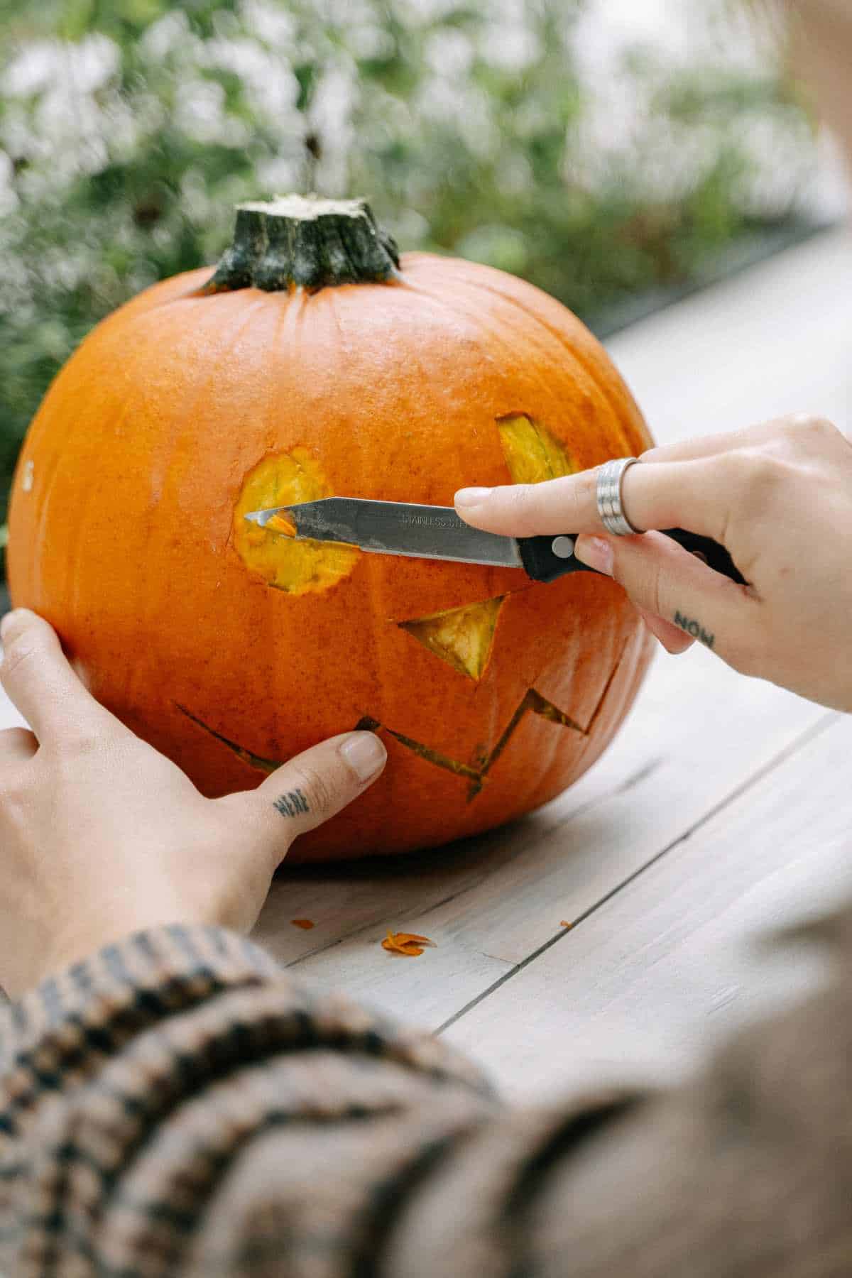 A person carving a jack-o'-lantern face into an orange pumpkin on a table using a knife.