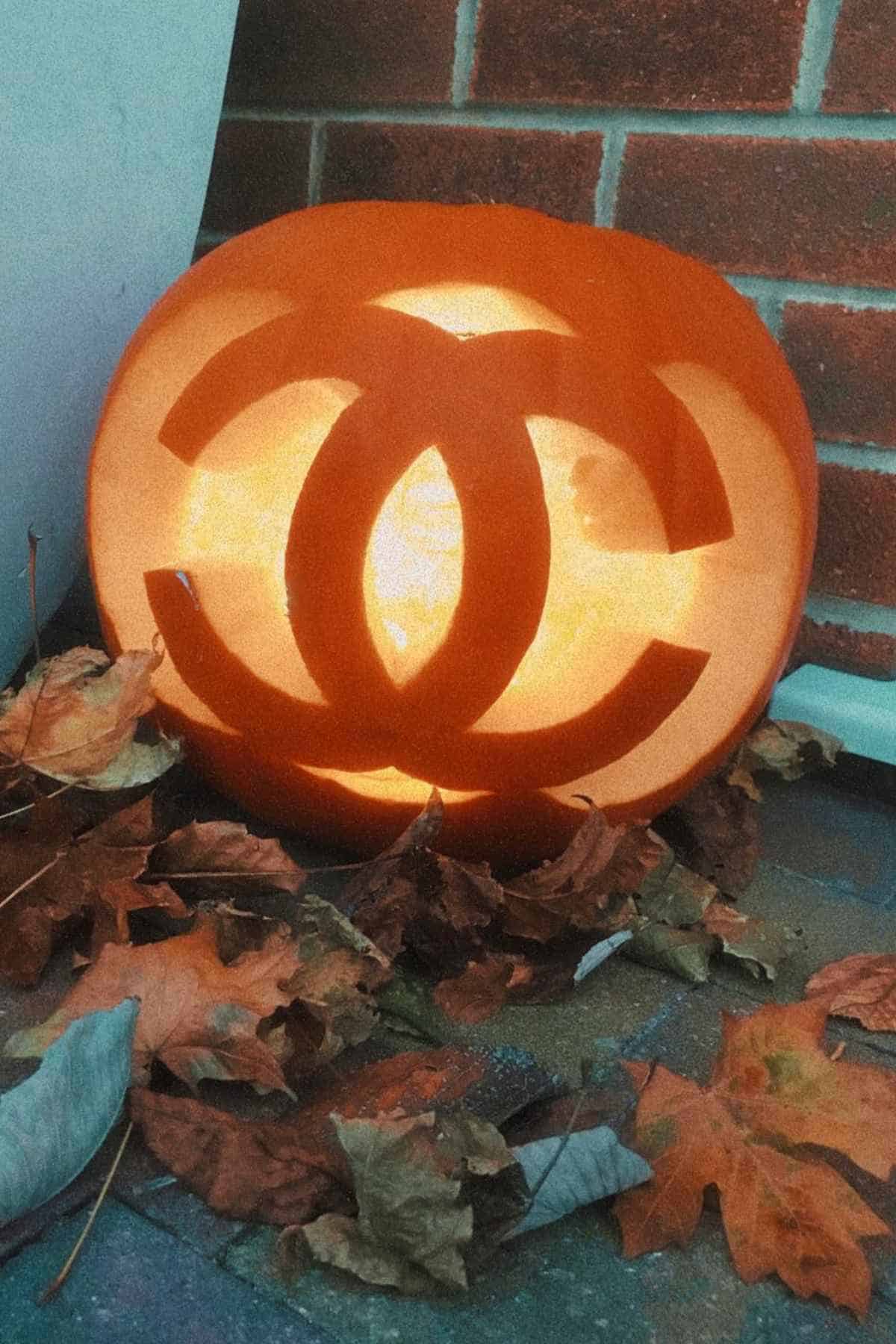 Pumpkin carved with an interlocking C design, placed on the ground surrounded by autumn leaves.