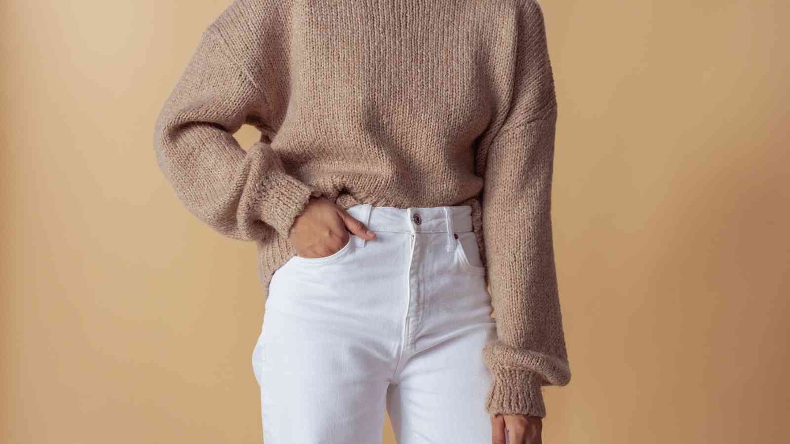 A person wearing a beige knit sweater and white pants.