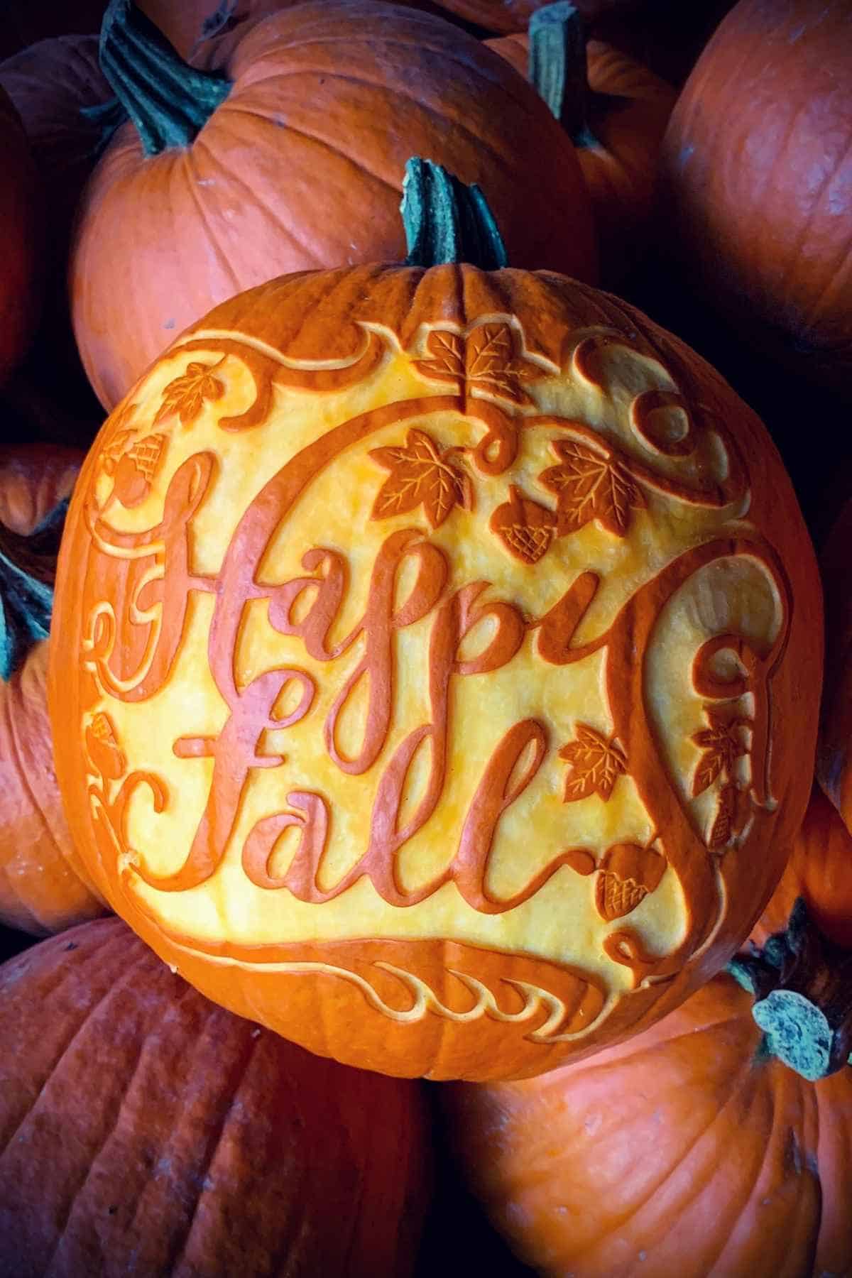 A pumpkin intricately carved with "Happy Fall" surrounded by autumn leaves and swirls.