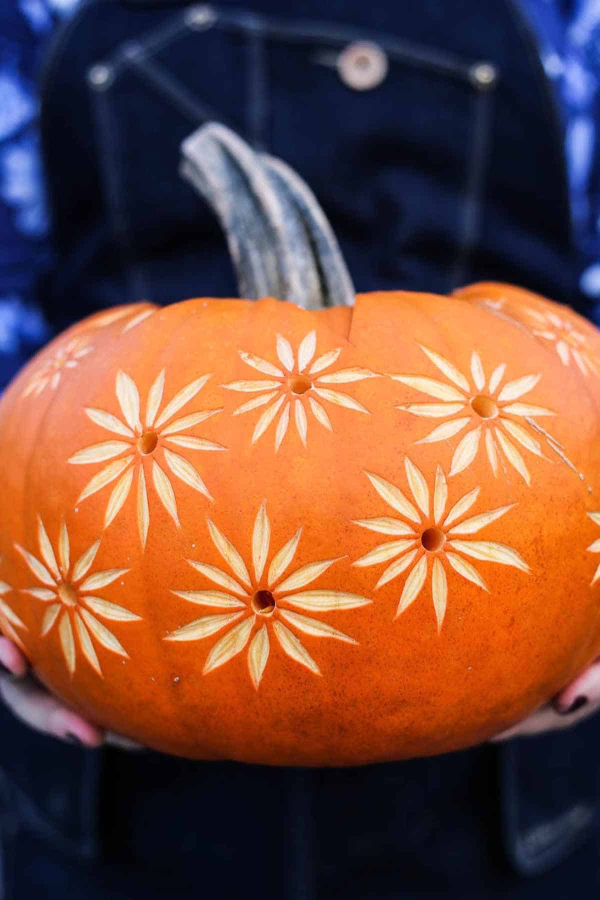 Pumpkin with carved star patterns being held in dark clothing background.