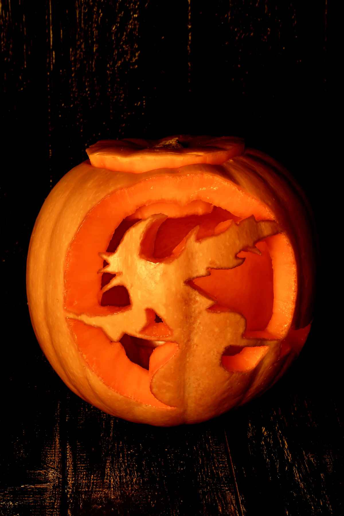 A pumpkin carved with a silhouette of a witch flying on a broomstick, illuminated from inside.