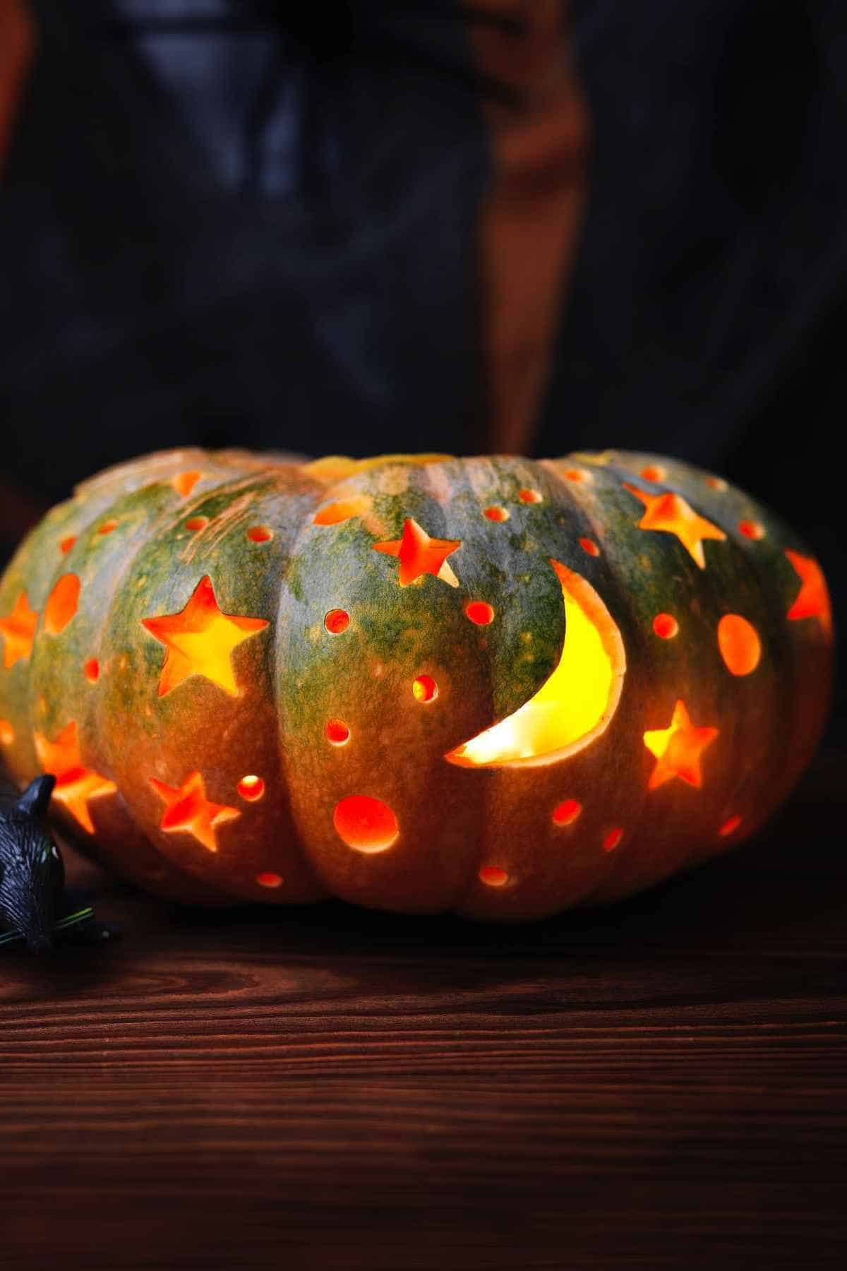 A carved pumpkin with star and moon cutouts emits a warm glow, resting on a wooden surface.