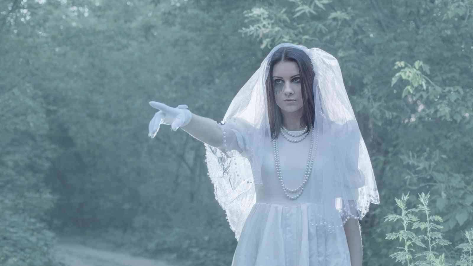 A person in a white dress and veil stands in a wooded area.
