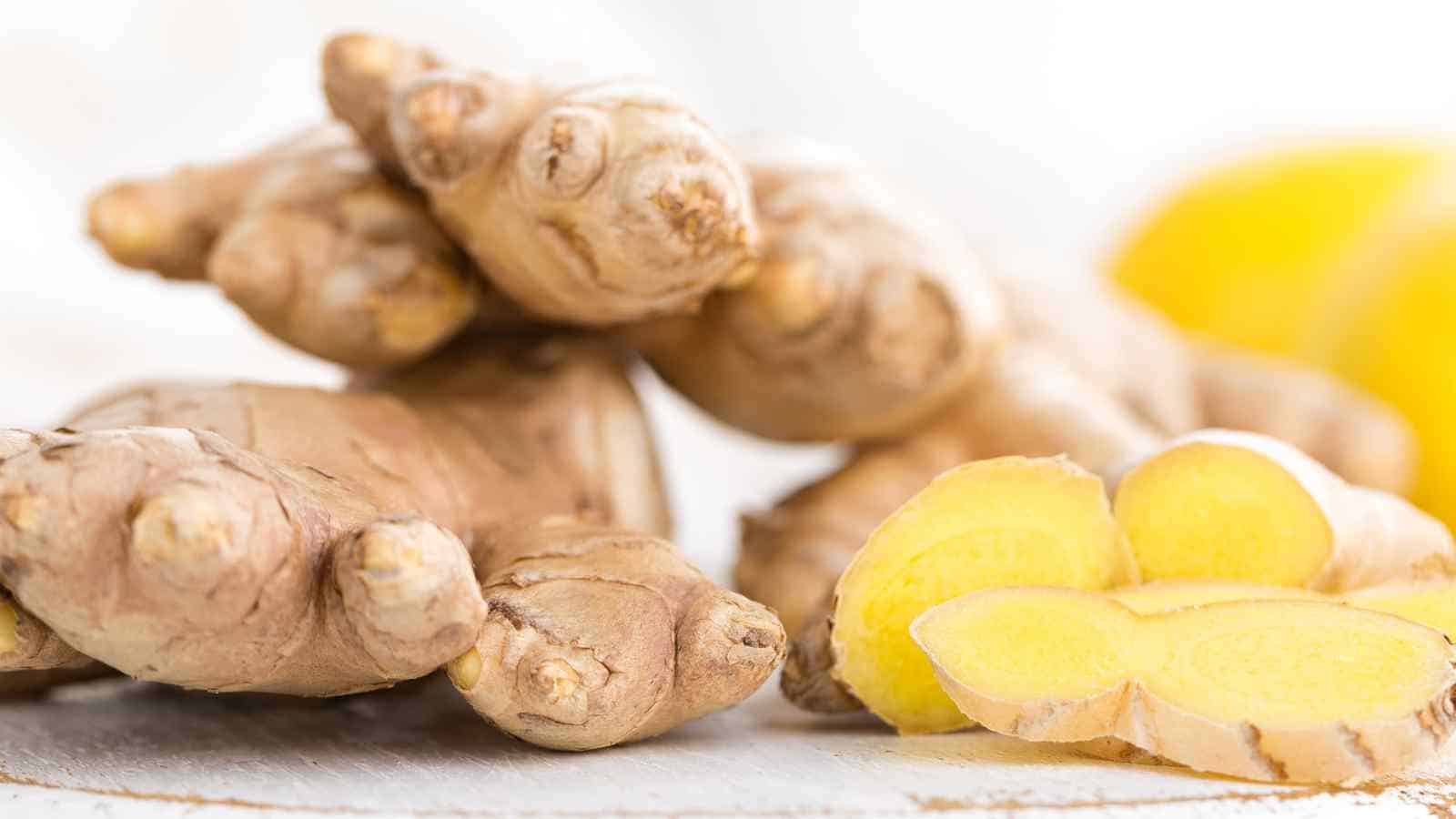 Close-up of fresh ginger root with a few sliced pieces on a light surface.