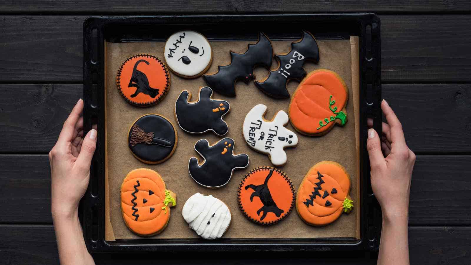 Hands holding a tray of Halloween-themed cookies.