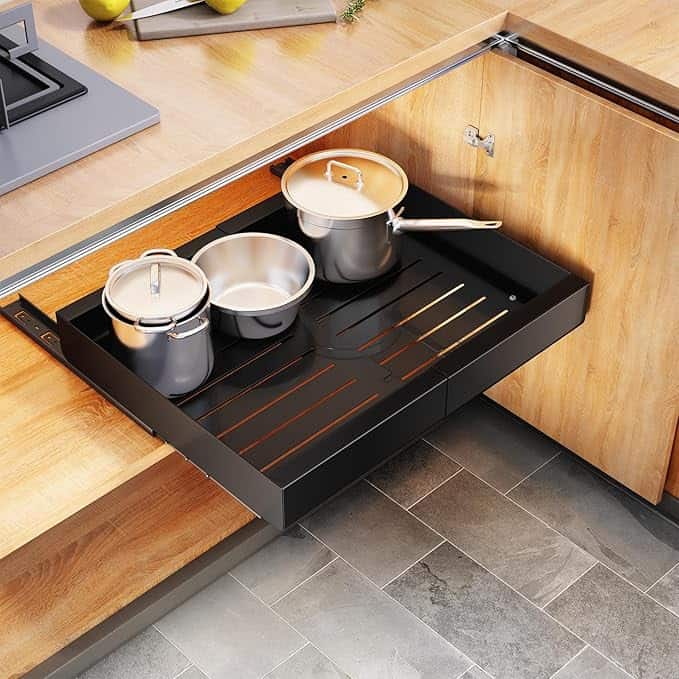 A kitchen drawer features a black pull-out tray with three pots of varying sizes on it.