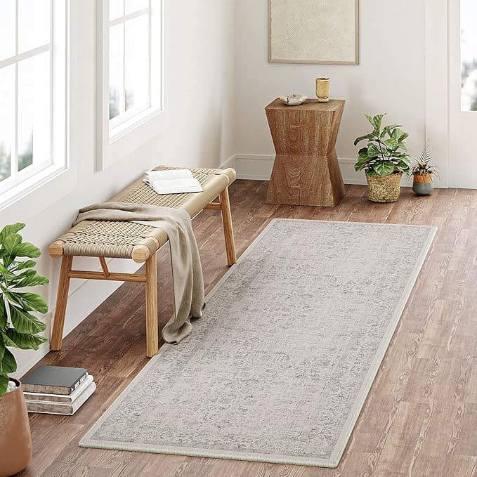 A light, patterned runner rug on brown wooden floor, beside a woven bench with a blanket.