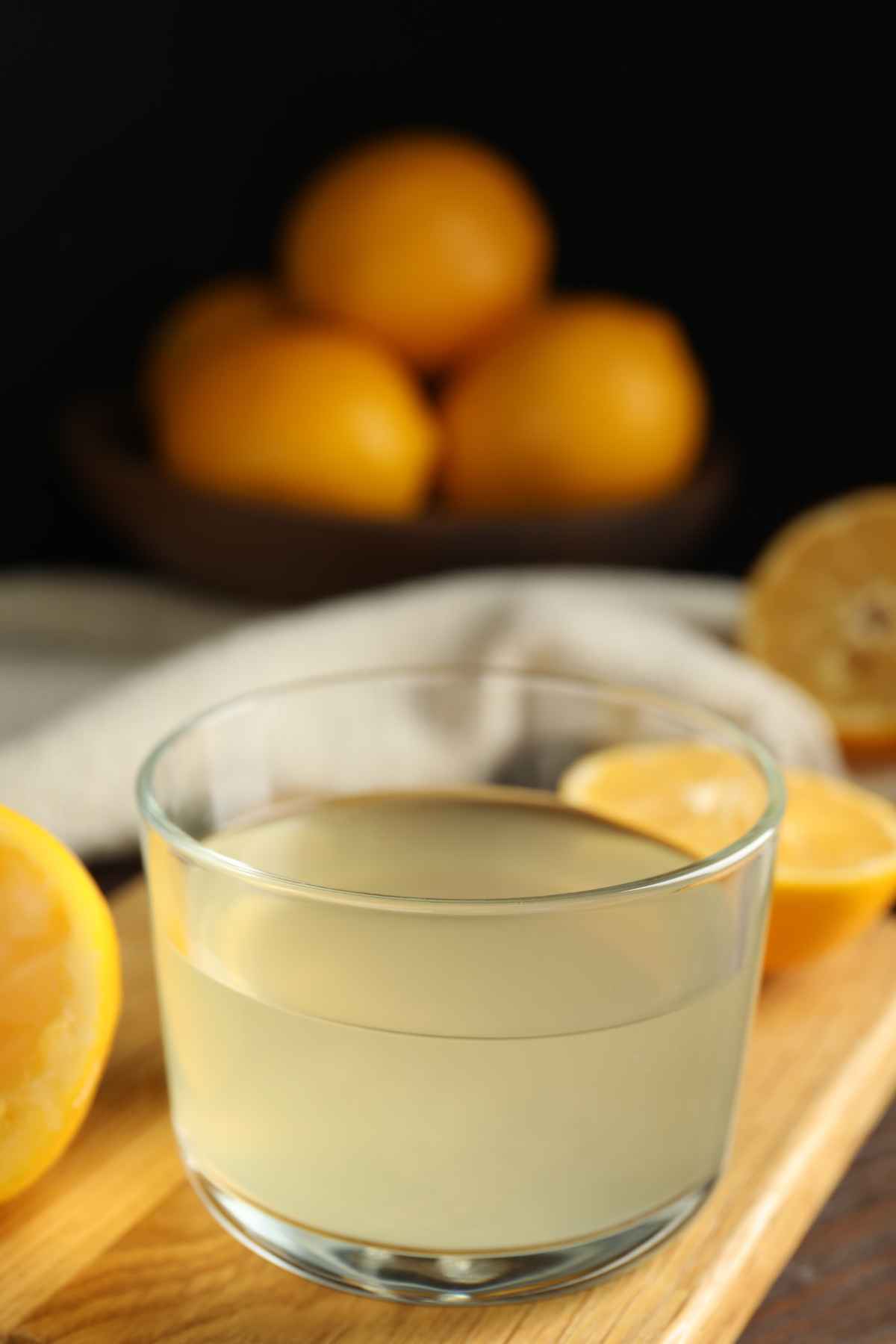 A bowl of lemon juice with a few stacks of lemon in the background.