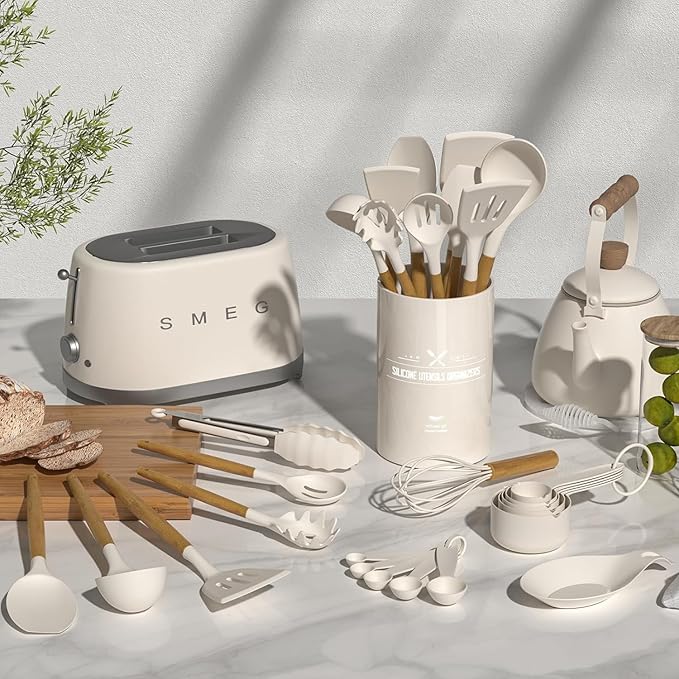 A collection of white kitchen utensils on a marble countertop includes a SMEG toaster, kettle, and various spoons and tools in a holder.