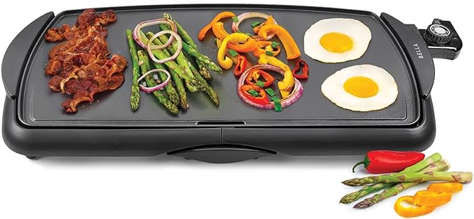 Electric griddle with bacon, asparagus, sliced bell peppers, and sunny-side-up eggs, with additional vegetables displayed in front.