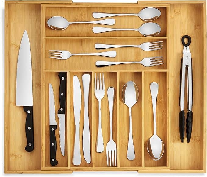 A wooden cutlery organizer with knives, forks, spoons, and tongs neatly arranged in compartments.
