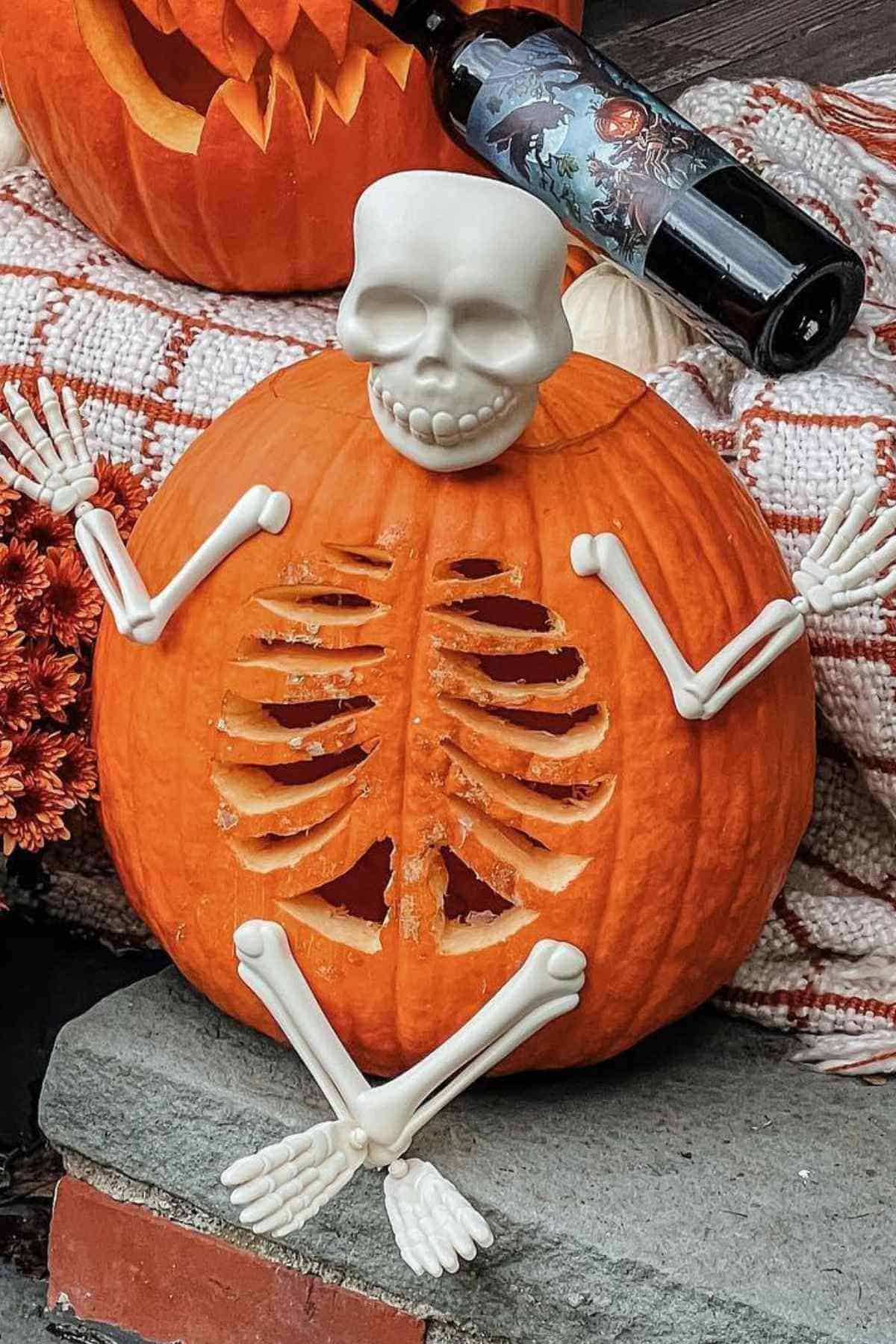 A carved pumpkin with skeleton arms and legs is sitting on a step. A decorative bottle is nearby.