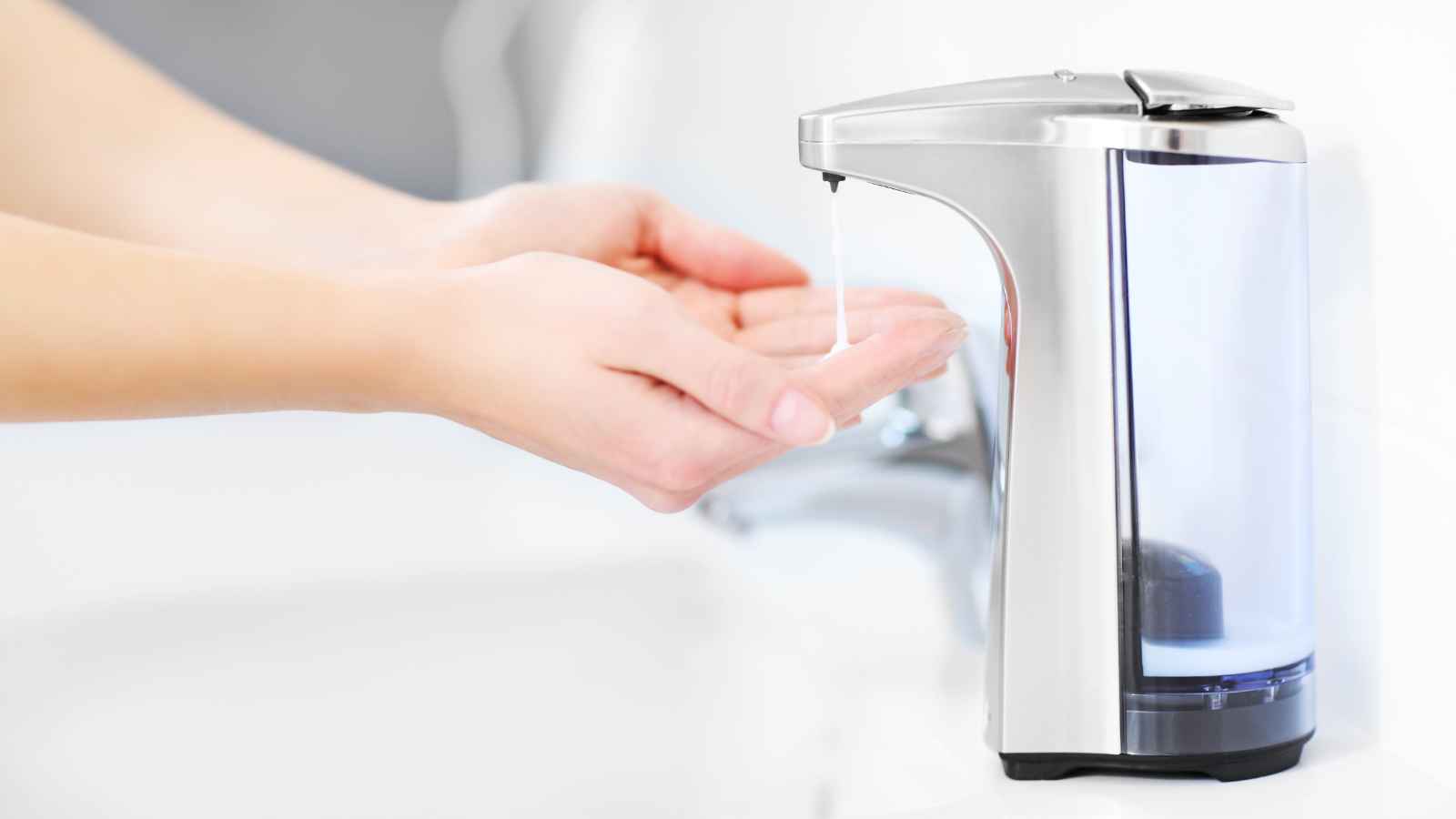 Hands positioned under an automatic soap dispenser with soap being dispensed.