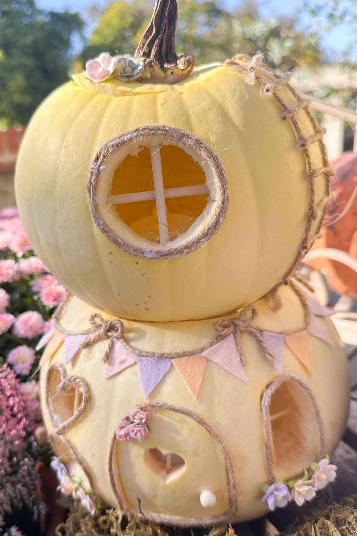 A whimsical house made from two stacked white pumpkins, adorned with small flowers, twine, and miniature windows and doors.