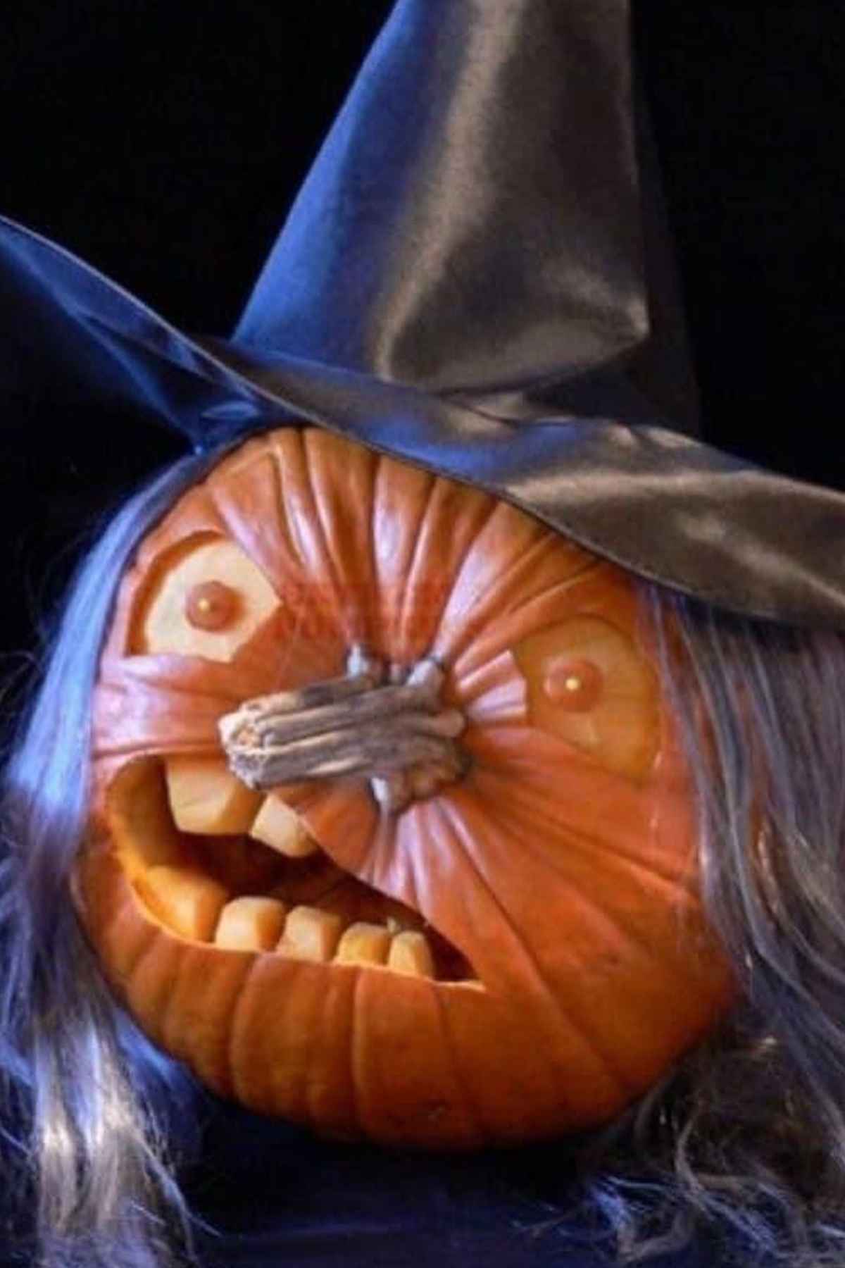 Pumpkin carved as a witch with a crooked nose, wearing a black pointed hat and sporting long gray hair.