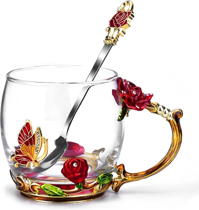 Glass mug adorned with red roses and butterfly design, accompanied by a decorated spoon.