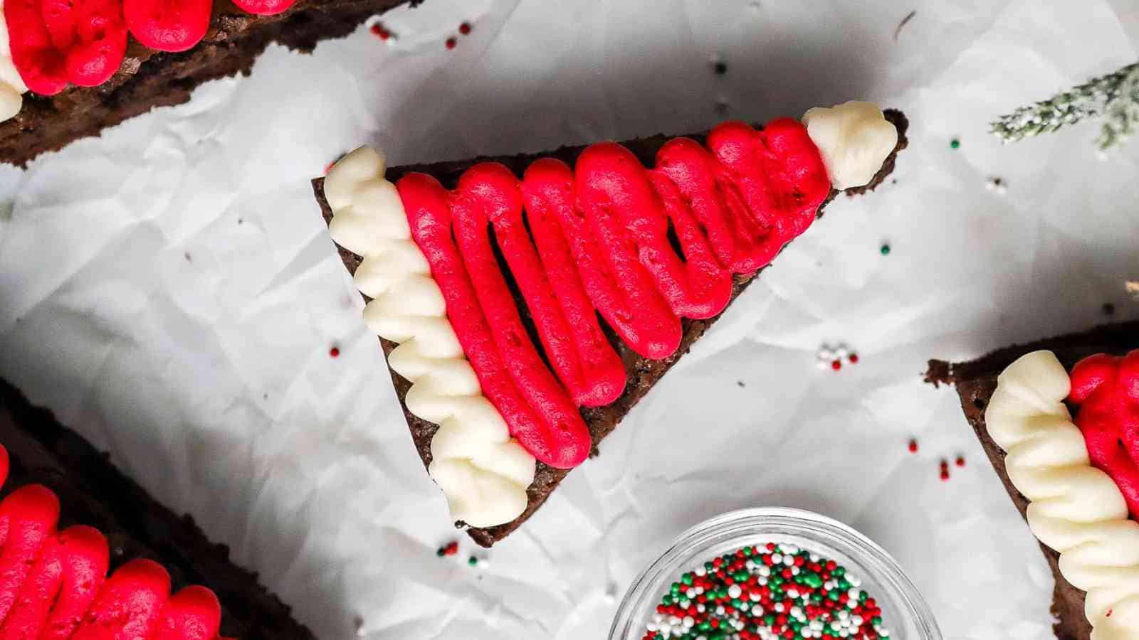 A Santa Hat Brownie, decorated with red and white icing, surrounded by sprinkles on a crumpled white background.