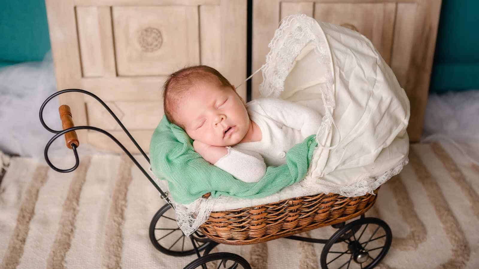 A newborn baby sleeps in a vintage wicker pram with a white canopy and green blanket, indoors on a striped rug—perfect inspiration for parents seeking noble boy names.