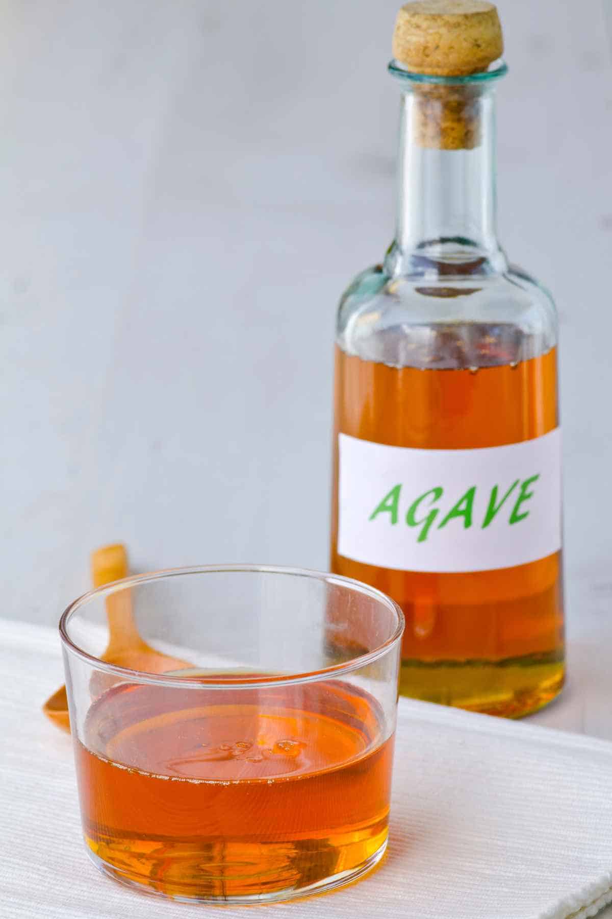 A bottle labeled "Agave" stands behind a glass filled with agave syrup.