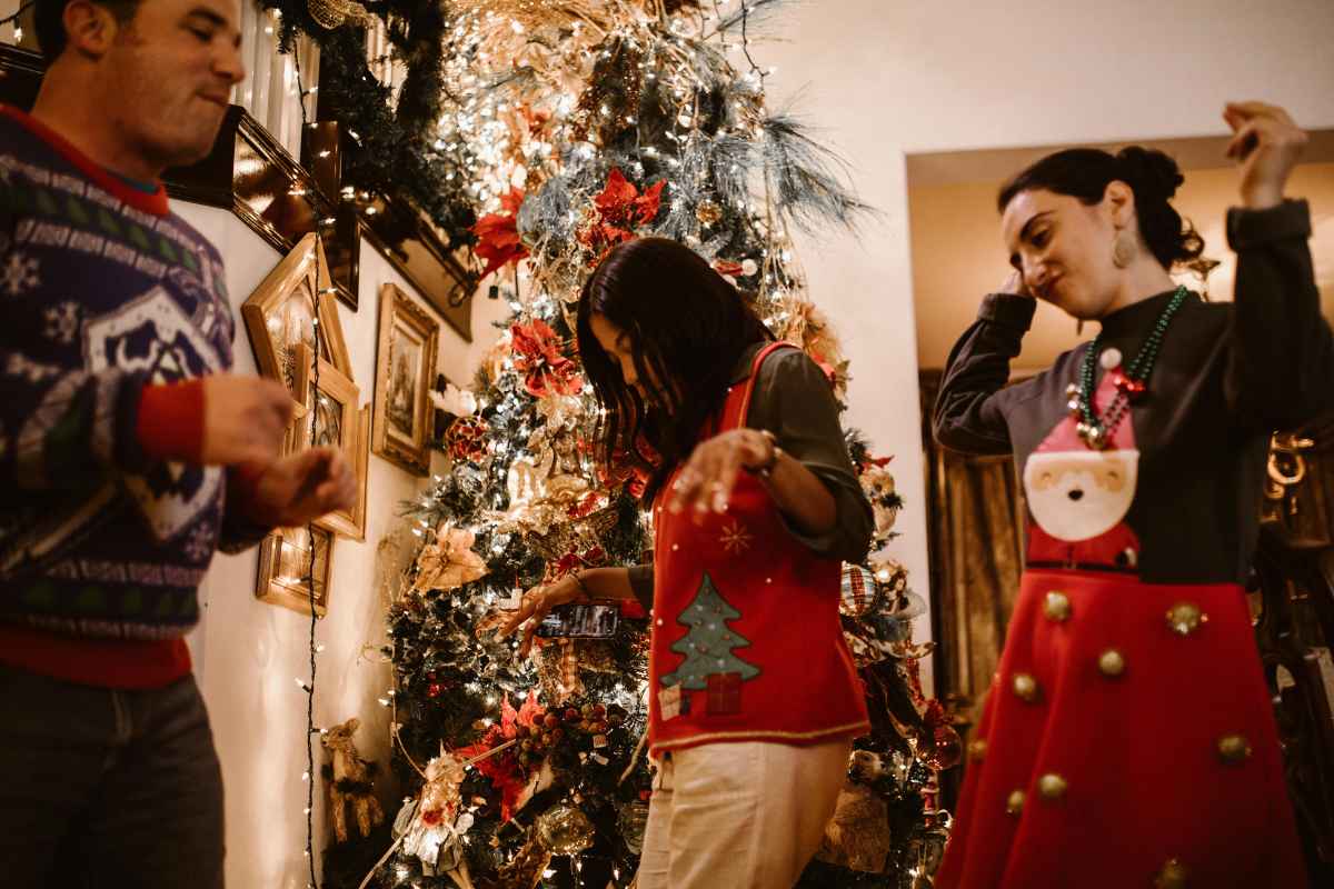 Three people clad in festive sweaters dance joyfully in front of a beautifully decorated Christmas tree, embodying the essence of heartwarming Christmas themes.
